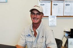 A man wearing glasses and a hat sitting in front of a wall.