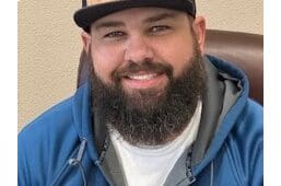 A man with a beard and hat smiling for the camera.